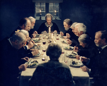 Das Bild zeigt eine Filmszene, in der 12 Menschen an einem reich gedeckten, festlichen Tisch sitzen und zu Abend essen.